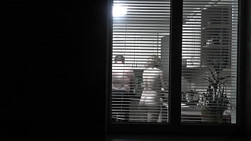 Peeping. Voyeur. Neighbor crank Spycam in evening on street looks out window as bare uber-sexy neighbor in kitchen preps dinner for her husband. bare in public. bare at home. Family.  Outdoor